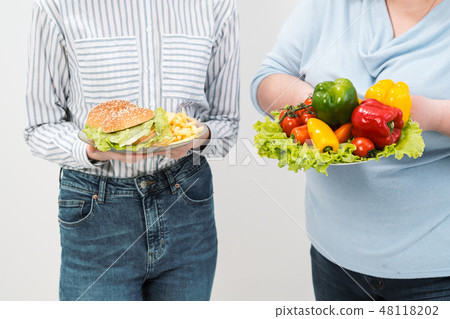 Two girls, thick and thin, with healthy food from vegetables and fruits and unhealthy fast food with Two girls, thick and thin, with healthy food from vegetables and fruits and unhealthy fast food with 48118202