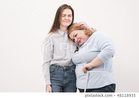 A fat woman measures her waist with a measuring tape in casual clothing on a white background. A fat woman measures her waist with a measuring tape in casual clothing on a white background. 48118935