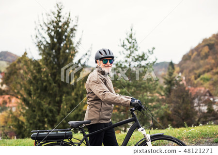 Active senior man with electrobike standing outdoors on a road in nature. 48121271