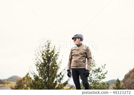 A portrait of active senior man with bicycle helmet standing outdoors in nature. A portrait of active senior man with bicycle helmet standing outdoors in nature. 48121272