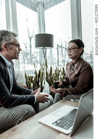 Dark-haired elegant woman in a brown satin blouse speaking in the office with her partner 48127899
