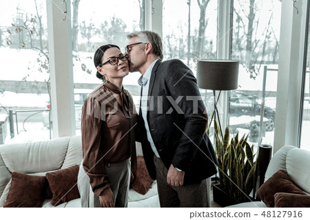 Tall grey-haired handsome man in a blue shirt kissing a woman on a cheek 48127916