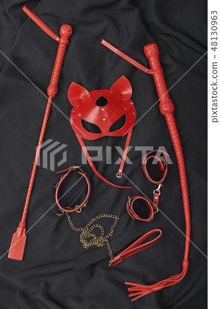 Couple Sexy Toys. Vertical photo of red bdsm leather set (handcuffs, whip, mask, chain) on a black 48130963