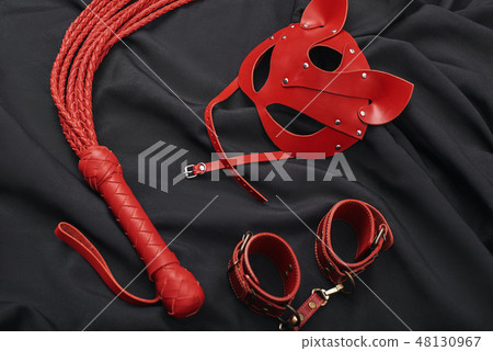 BDSM Sexual Practice. Top view of red bdsm leather set (handcuffs, whip, mask) on a black silk 48130967