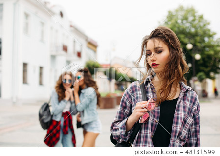 Jealous girls whispering about third girl in front 48131599