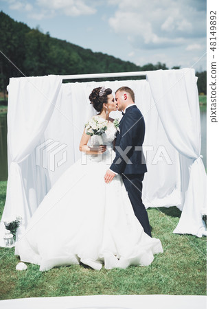 Stylish couple of happy newlyweds walking in the park on their wedding day with bouquet Stylish couple of happy newlyweds walking in the park on their wedding day with bouquet 48149892