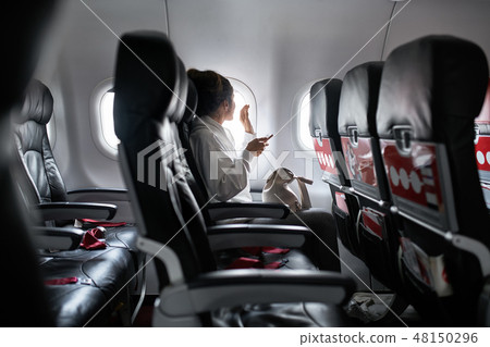 Woman with smartphone sits on black seat in plane Woman with smartphone sits on black seat in plane 48150296
