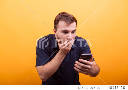 Portrait of shocked young man looking at mobile phone isolated on yellow background Portrait of shocked young man looking at mobile phone isolated on yellow background 48152418