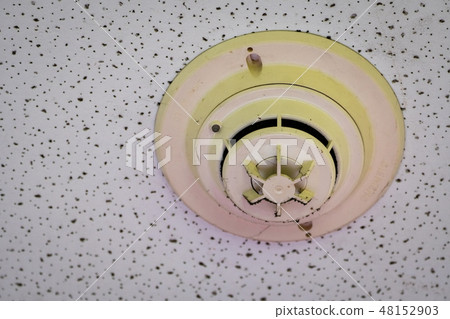 Old smoke detector with cobwebs on ceiling wall. 48152903