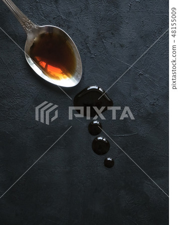 Spoon with leaking soy sauce on the black table. 48155009