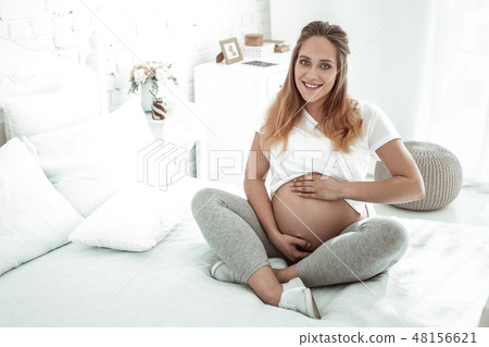 Smiling future mother lifting her t-shirt and presenting round stomach 48156621