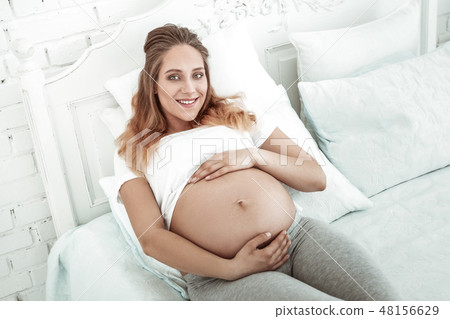 Pleasant woman with wide smile wrapping pregnant belly 48156629