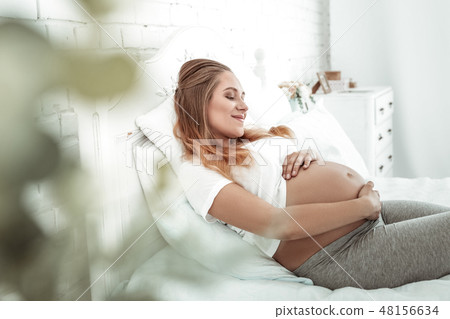 Tranquil long-haired pregnant woman touching her smooth stomach Tranquil long-haired pregnant woman touching her smooth stomach 48156634