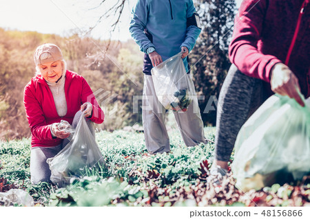 Retired woman wearing gloves while cleaning the forest from garbage Retired woman wearing gloves while cleaning the forest from garbage 48156866