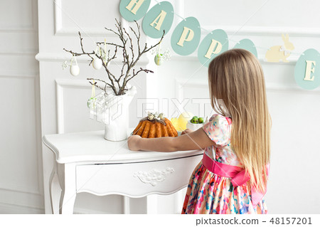A blonde girl in a beautiful colored dress is standing with her back to the festive table holding a A blonde girl in a beautiful colored dress is standing with her back to the festive table holding a 48157201