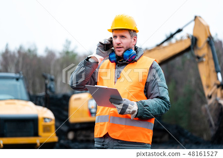Portrait of a quarry worker standing in front of excavator 48161527
