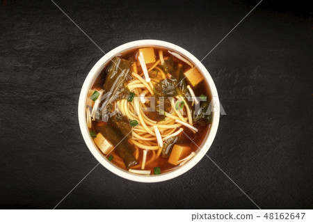 A photo of a bowl of miso soup with tofu, scallions, noodles, wakame, and enoki mushrooms, shot from 48162647
