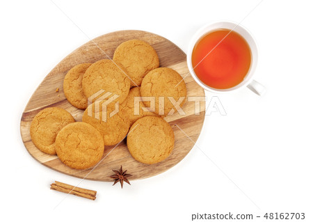 A photo of ginger cookies with a cup of tea, a cinnamon stick, and an anise star, shot from the top 48162703