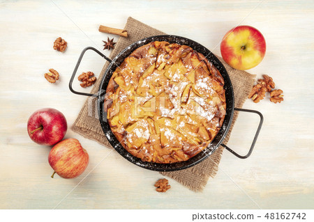 A photo of an apple pie in a pan, shot from the top on a rustic wooden background with apples A photo of an apple pie in a pan, shot from the top on a rustic wooden background with apples 48162742