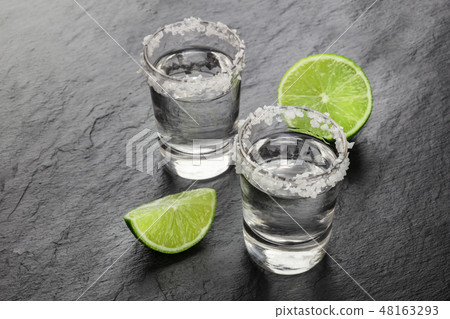 A photo of a tequila shots with lime slices on a black background with copy space 48163293