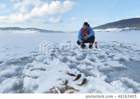 Fisherman catching fish on a frozen lake  48163405