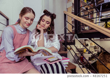 Calm and peaceful girls sitting shoulder to shoulder and reading book Calm and peaceful girls sitting shoulder to shoulder and reading book 48167251