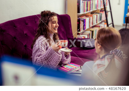 Laughing girls sitting on violet velvet couch surrounded with books 48167620