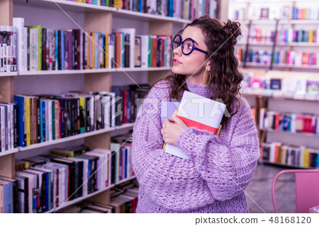 Long-haired appealing girl in oversize sweater carrying bunch of books Long-haired appealing girl in oversize sweater carrying bunch of books 48168120