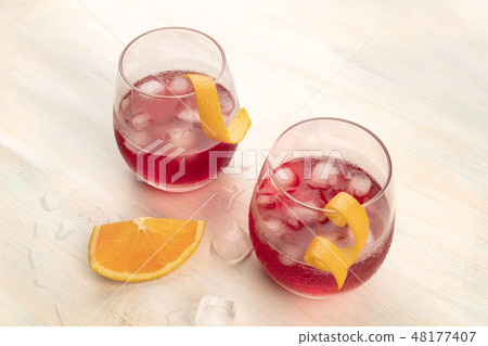 Two vibrant cocktails with campari and orange zest garnishes, with ice cubes on a light background Two vibrant cocktails with campari and orange zest garnishes, with ice cubes on a light background 48177407