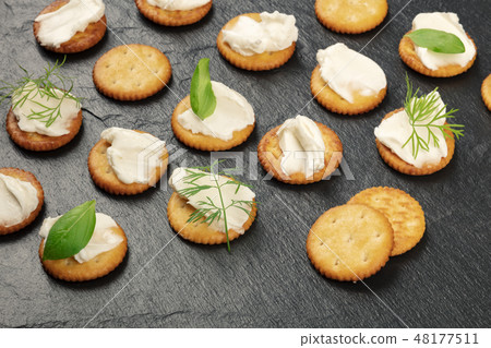 A photo of salt crackers with soft spreadable cream cheese and herbs on a black background with copy 48177511