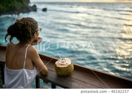 Woman in glasses looking at sunset sea in outdoor cafe Woman in glasses looking at sunset sea in outdoor cafe 48182257