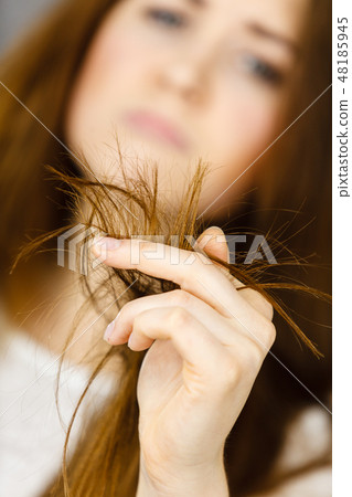 Worried woman looking at her dry hair ends 48185945