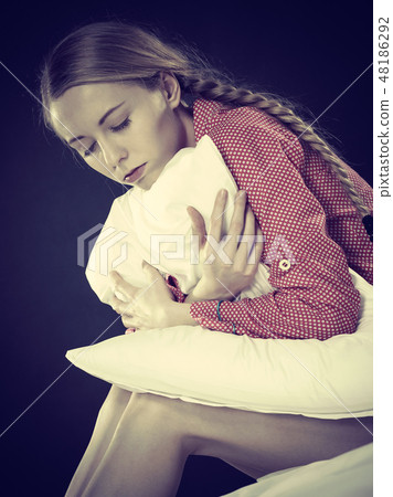 Sad depressed girl in bed gripping pillow Sad depressed girl in bed gripping pillow 48186292