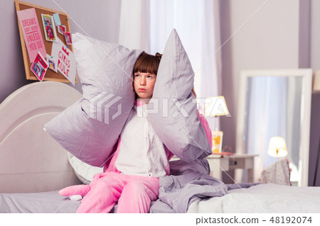Bored schoolgirl covering her ears with pillows Bored schoolgirl covering her ears with pillows 48192074