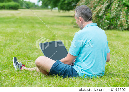 Man working on his laptop in the park Man working on his laptop in the park 48194502