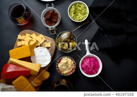 Wooden board with various types of cheese and snacks and two glasses of red wine on black table Wooden board with various types of cheese and snacks and two glasses of red wine on black table 48197108