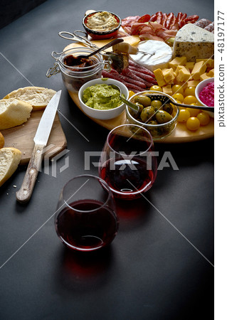 Antipasti board with cheese and meat snacks with red wine and baguette on board on black table 48197177
