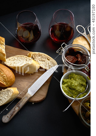 Antipasti board with cheese and meat snacks with red wine and baguette on board on black table Antipasti board with cheese and meat snacks with red wine and baguette on board on black table 48197180