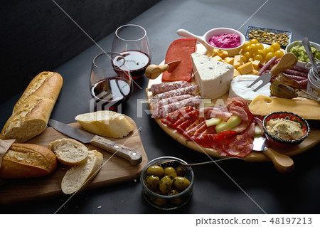 Antipasti board with cheese and meat snacks with red wine and baguette on board on black table 48197213