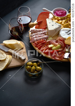 Antipasti board with cheese and meat snacks with red wine and baguette on board on black table 48197216