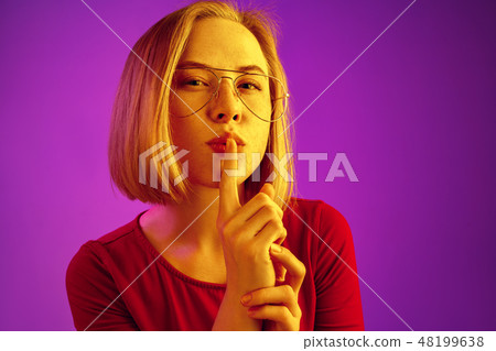 The young woman calling for silence over neon background The young woman calling for silence over neon background 48199638