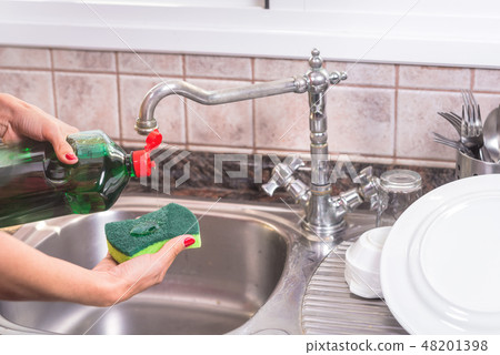 woman with red manicure putting detergent in the scourer, to wash the dishes. 48201398