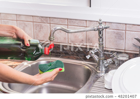 woman with red manicure putting detergent in the scourer, to wash the dishes. 48201407