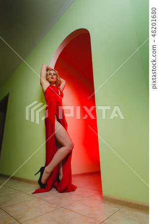 Attractive blonde model in the red dress with high slit and long naked legs 48201680
