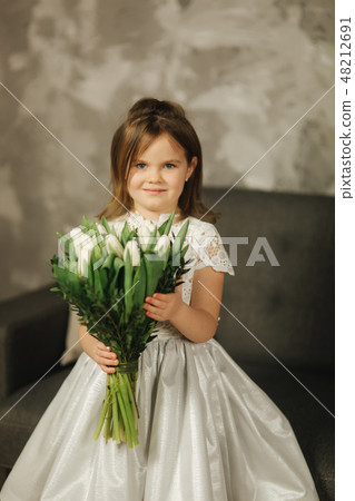 Beautiul little girl hold a bouquet of flowers at home. She sist on sofa at home and waiting for her Beautiul little girl hold a bouquet of flowers at home. She sist on sofa at home and waiting for her 48212691