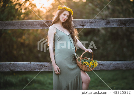 Pregnant pretty woman is wearing wreath of yellow dandelion flowers over sunset lights , spring time Pregnant pretty woman is wearing wreath of yellow dandelion flowers over sunset lights , spring time 48215852