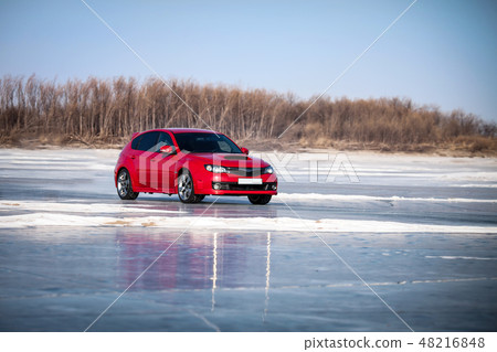 Red car moving by ice of frozen river 48216848