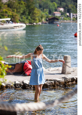 girl sits on a wooden pier and soaks her feet in the water. Summer Sunny day by the sea. Vacation 48220059