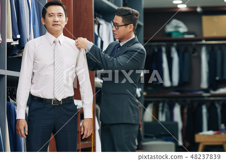 Shop assistant measuring customer Shop assistant measuring customer 48237839