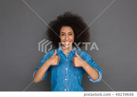Freestyle. Mulatto woman standing isolated on grey showing thumbs up smiling cheerful 48239686